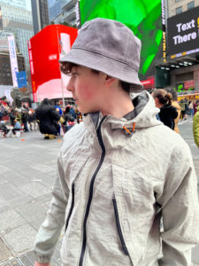 Young man wearing taupe windbreaker and a grey bucket hat