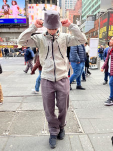 Grey hat, windbreaker, pants against Times Square backdrop