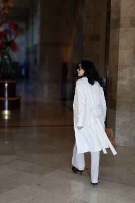 Model walking into a building foyer wearing a white cardigan and pants