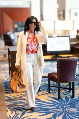 Model walking through hotel lobby wearing white cardigan and pants