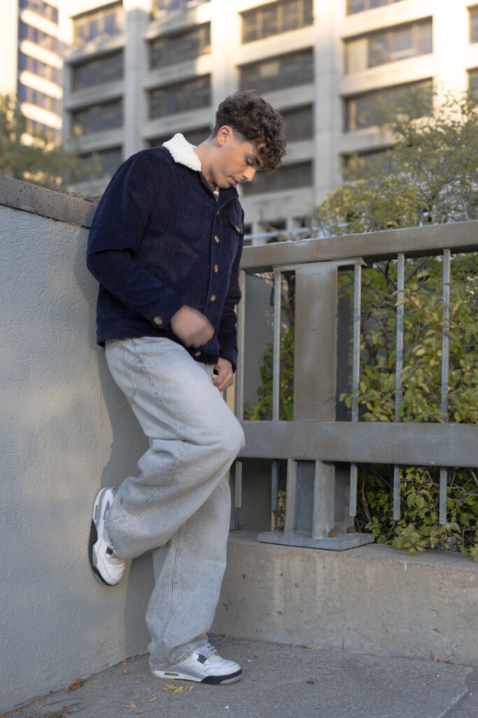 model wearing navy corduroy jacket with white faux fur lining and collar and grey jeans leans against concrete wall