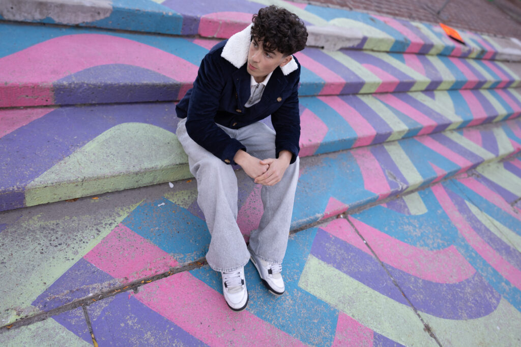 model wearing navy corduroy jacket with white faux fur lining sits on stairs painted in colourful graffiti