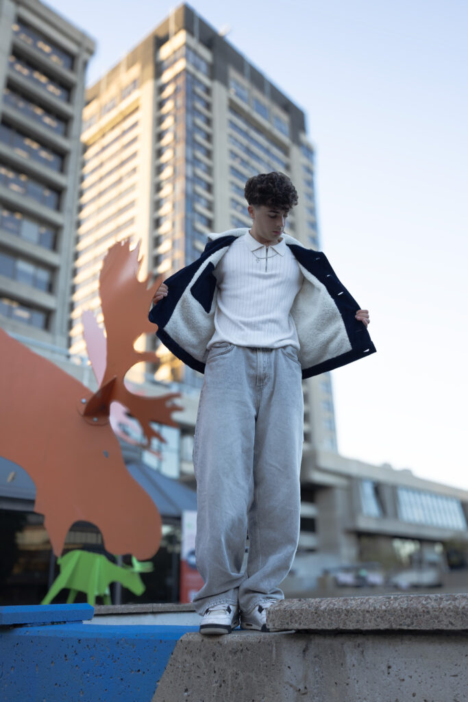 model wearing navy corduroy jacket with white faux fur lining, grey jeans, white polo shows the inside of the jacket